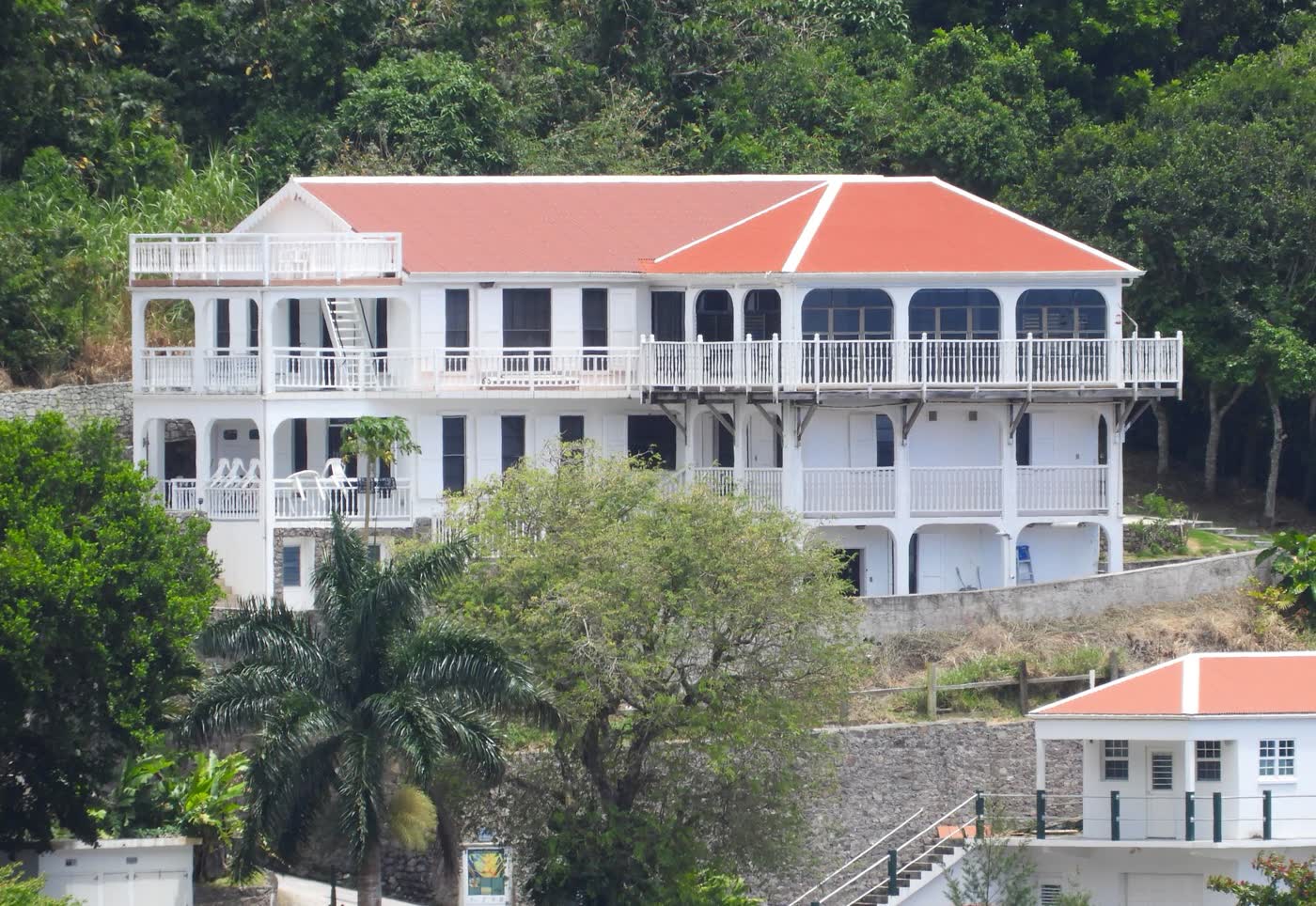 A three-story Saban villa with a red roof and wraparound verandas set against green hillside